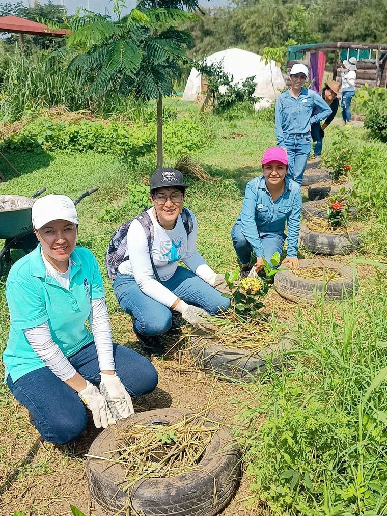 Grupo de mujeres sonriendo mientras siembran en camas de llantas